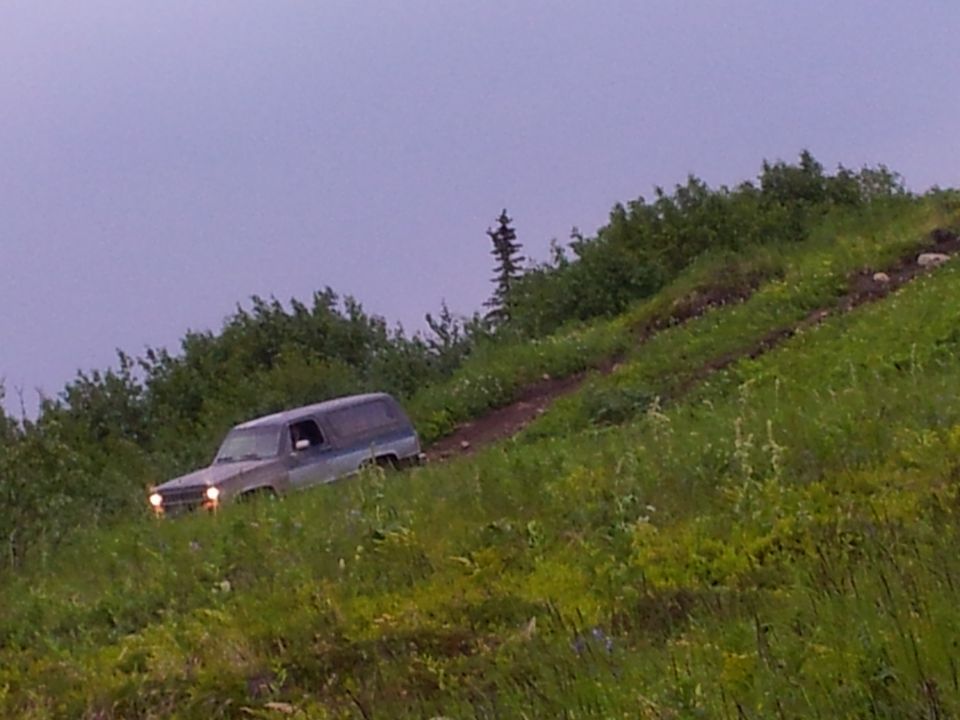 Gray 1990 Chevrolet Suburban driving up a grassy hill on a dirt path