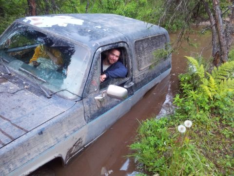 1990 Chevrolet Suburban - A man smiles from the driver's seat of a mud-covered Chevrolet K5 Blazer submerged in water.