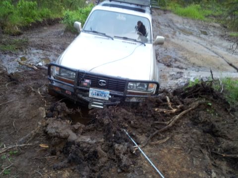 1990 Chevrolet Suburban - This silver SUV, possibly a 1998 Toyota Land Cruiser, is deeply stuck in mud with its front bumper winch engaged.
