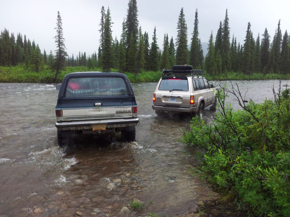 1990 Chevrolet Suburban and a Toyota Land Cruiser driving through a river