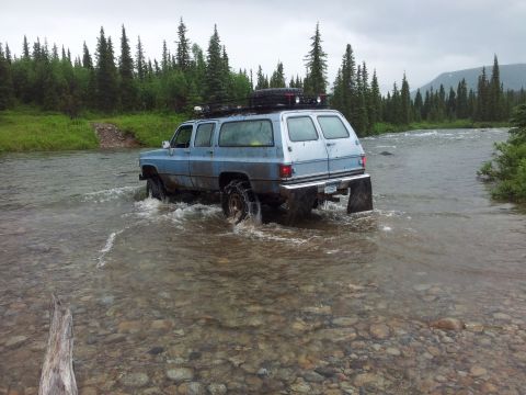 1990 Chevrolet Suburban - Blue 1990 Chevrolet Suburban crossing a rocky riverbed in a wooded area.