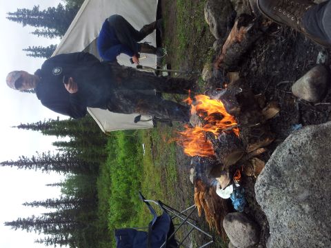 1990 Chevrolet Suburban - A group of people are gathered around a campfire in a wooded area, with tents set up in the background.
