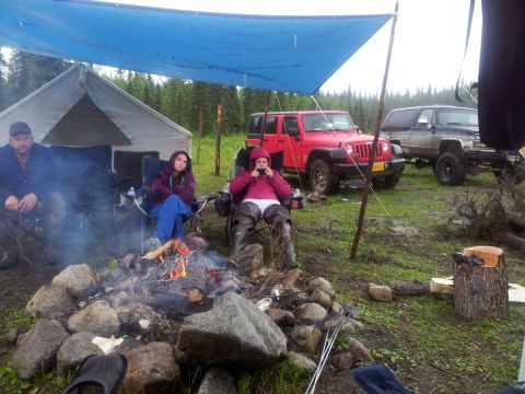 1990 Chevrolet Suburban - People sit around a campfire at a campsite with two off-road vehicles parked nearby.
