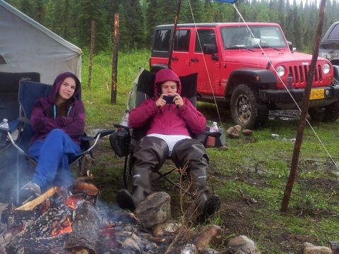 1990 Chevrolet Suburban - A red Jeep Wrangler is parked at a campsite next to two people relaxing by a campfire.