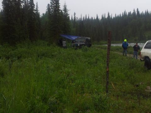 1990 Chevrolet Suburban - Two SUVs and a campsite are visible near a riverbank with trees in the background.