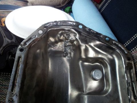 1990 Chevrolet Suburban - This oil pan has sustained significant damage, with a large dent and bent metal near the drain plug.
