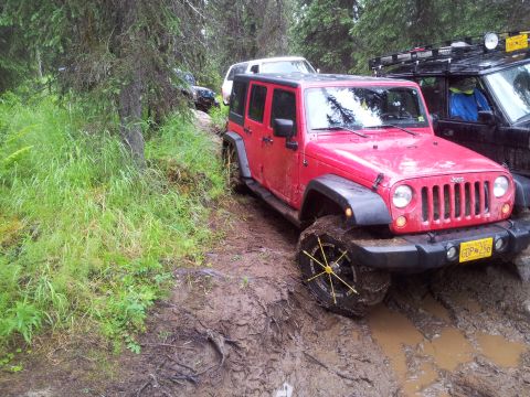 1990 Chevrolet Suburban - Several off-road vehicles navigate a muddy path through a dense forest.
