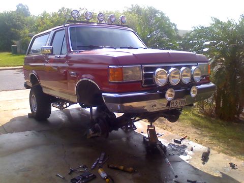 1990 Ford Bronco - This lifted Ford Bronco is undergoing maintenance with its front end raised on jacks and tools scattered around.