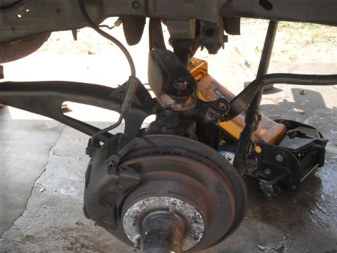 1990 Ford Bronco - Close-up of a vehicle's suspension and brake components, with a jack in the background.