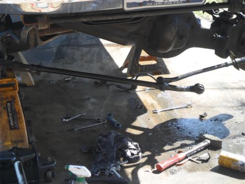 1990 Ford Bronco - Undercarriage components, including steering linkage and suspension parts, are visible with tools scattered around.