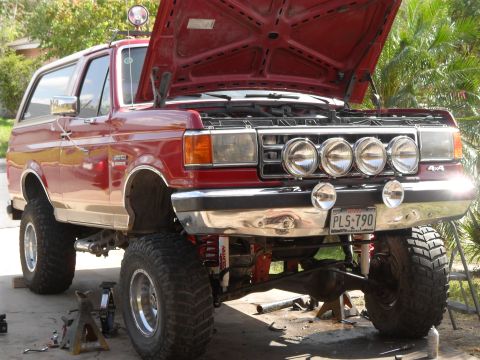 1990 Ford Bronco - This lifted SUV is undergoing maintenance with its hood and front end raised for access.