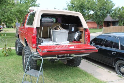 1990 Ford Bronco - Rear view of a red 1990 Ford Bronco loaded with camping gear, parked next to another vehicle.