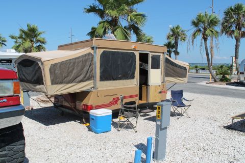 1990 Ford Bronco - A pop-up camper is parked at a campsite with chairs and a cooler outside.