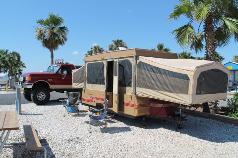 1990 Ford Bronco - A lifted red 1990 Ford Bronco is parked next to a pop-up camper at a campsite.