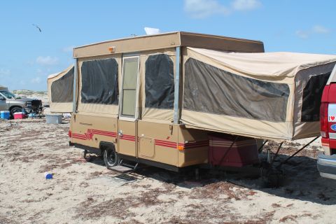 1990 Ford Bronco - A pop-up camper trailer is set up on a sandy beach next to a red truck under a clear blue sky.