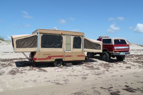 1990 Ford Bronco - 1990 Ford Bronco towing a pop-up camper on a beach under a blue sky.