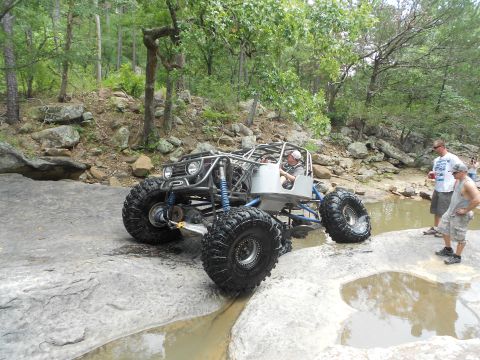 1967 Ford Mustang - A custom-built buggy with oversized tires is shown traversing a rocky, wet terrain with onlookers nearby.