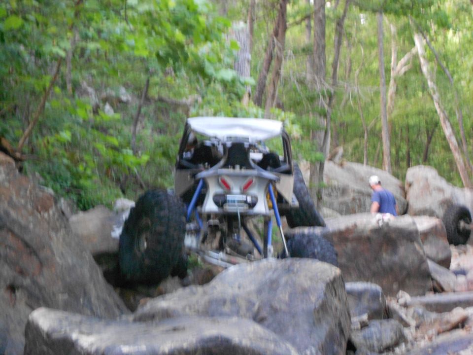 Off-road buggy with large tires navigating rocky terrain, rear view