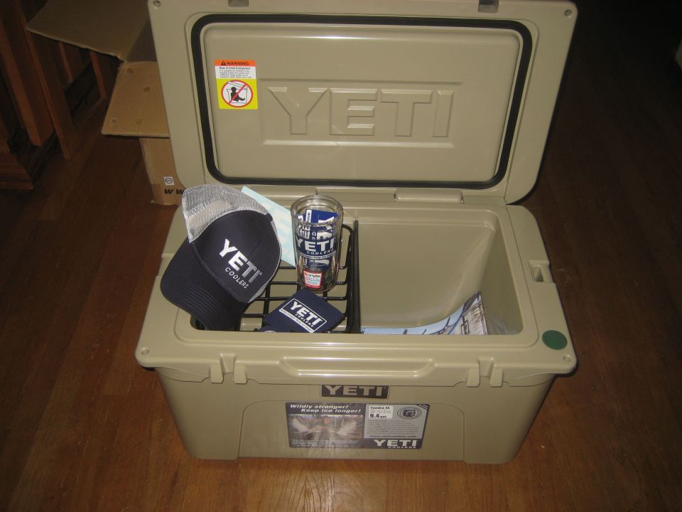 Tan Yeti cooler open with a navy Yeti hat, a Yeti cup, and a small Yeti bag inside