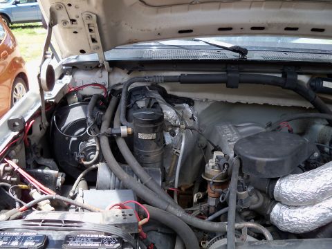 1995 Ford Bronco - Close-up of an engine bay, focusing on AC system parts and the battery.
