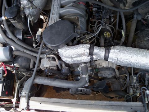 1995 Ford Bronco - Close-up view of an engine bay, showing various components including an alternator and an exhaust pipe covered in aluminum insulation.