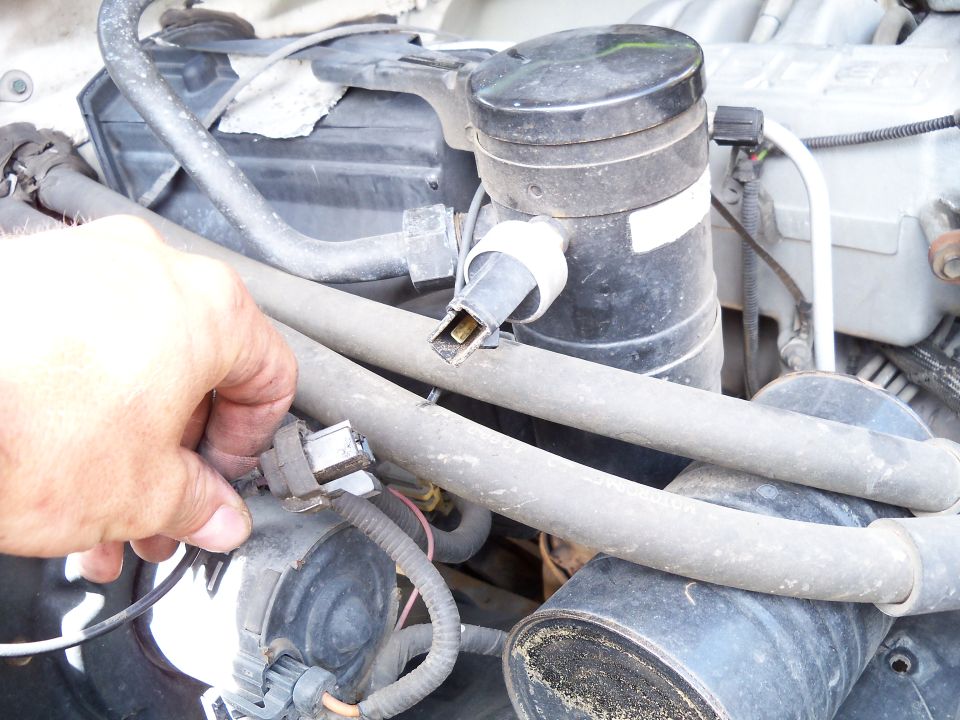 Close-up of engine bay hoses and connectors, with a hand visible on the left