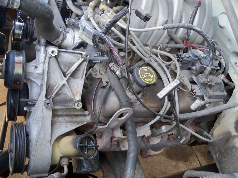 Engine bay with AC compressor and lines removed, showing hoses and belts