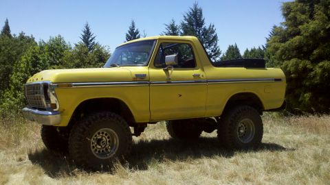 1978 Ford Bronco - This lifted 1978 Ford Bronco is shown in a three-quarter front view, parked in a grassy field with trees in the background.