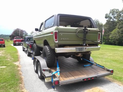 1979 Ford Bronco - A green Ford Bronco is being towed on a trailer, with other trucks visible in the background.