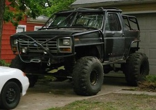 1986 Ford Bronco - This heavily modified black SUV features a prominent roll cage and oversized tires, suggesting off-road use.