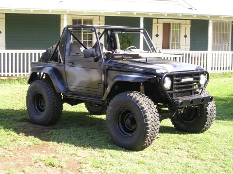 1987 Suzuki Samurai - This heavily modified SUV features large off-road tires and a prominent roll cage, parked in front of a residential building.
