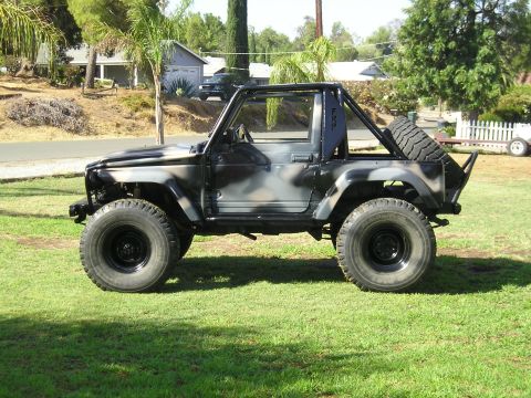 1987 Suzuki Samurai - A modified Suzuki Samurai with a camouflage paint job and off-road tires sits on a grassy lawn.