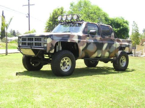1987 Suzuki Samurai - Modified pickup truck with camouflage paint and off-road lights sits on a grassy lawn.