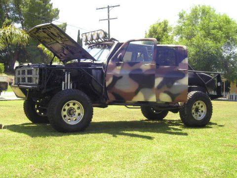 1987 Suzuki Samurai - A heavily modified pickup truck with camouflage paint sits on a grassy lawn.