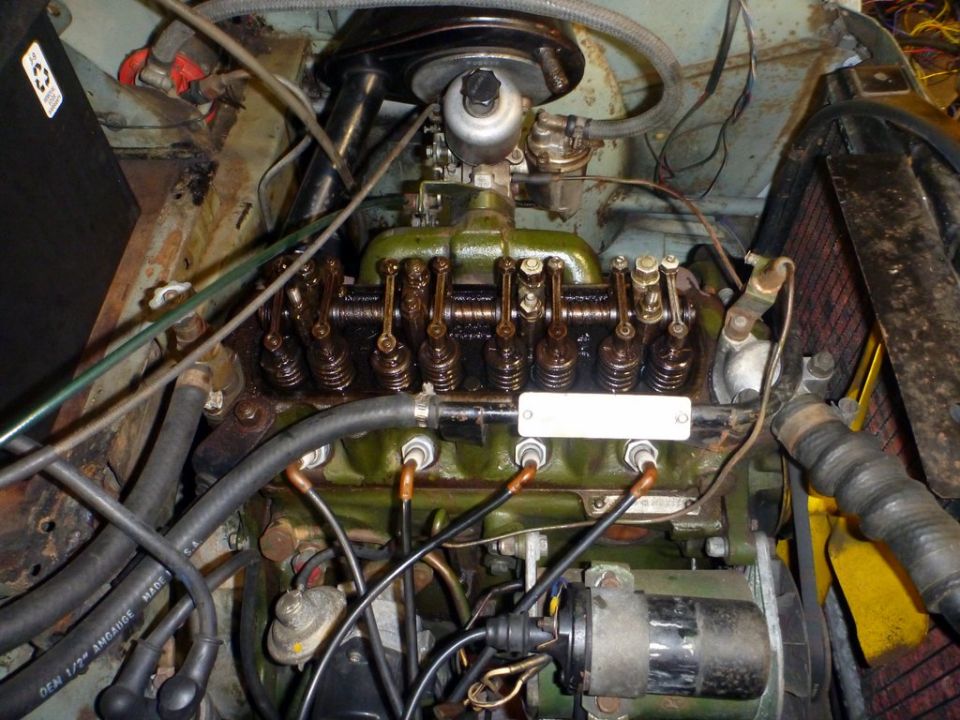 Close-up of a car's engine bay, showing the valve cover, carburetor, and spark plug wires