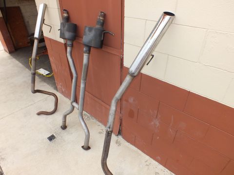 2003 Ford Crown Victoria - Exhaust components leaning on a wall, one bright polished tip among raw pipes.