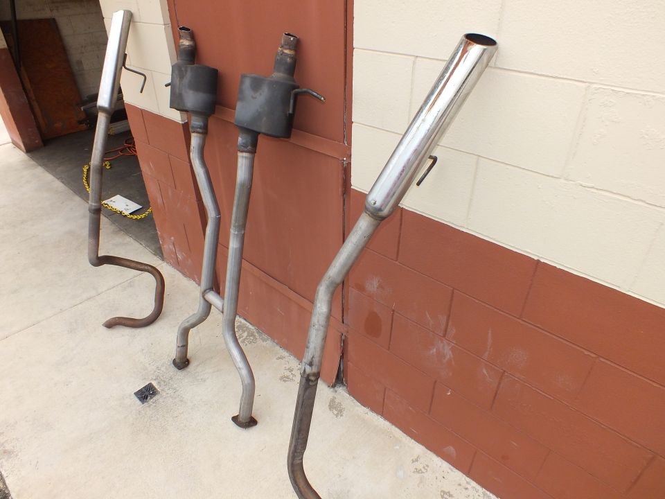 Dual exhaust pipes with mufflers and one chrome polished tailpipe against brick wall