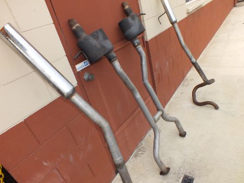 2003 Ford Crown Victoria - Exhaust pipes and mufflers stood against a brick wall, one polished tip visible.