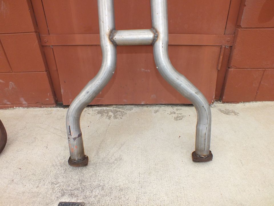 Aluminized exhaust H-pipe crossover and dual tailpipes against red brick wall
