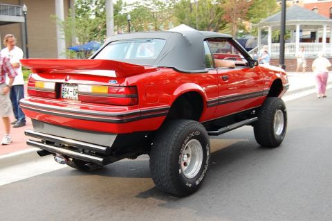 2007 Ford Mustang - This red convertible features a lifted suspension and oversized tires, altering its original appearance.