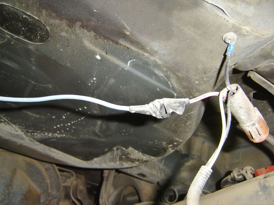 Close-up of a taped automotive wiring harness with connectors under a vehicle