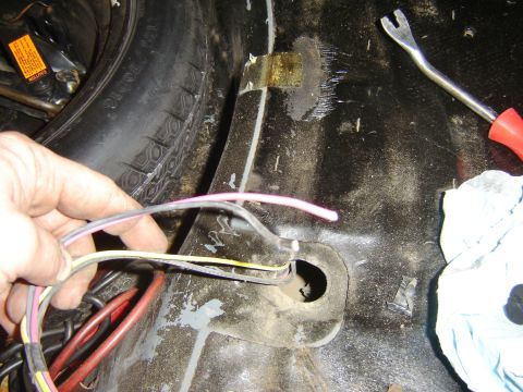 1987 Ford Mustang - A hand holds a wiring harness in the spare tire well of a vehicle, with a trim removal tool visible.