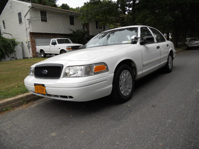 White Ford Crown Victoria parked on street, front 3/4 view. License plate is visible