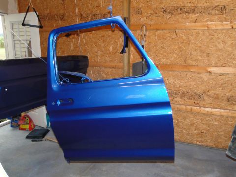 1978 Ford Bronco - A freshly painted blue car door is suspended for inspection in a workshop.