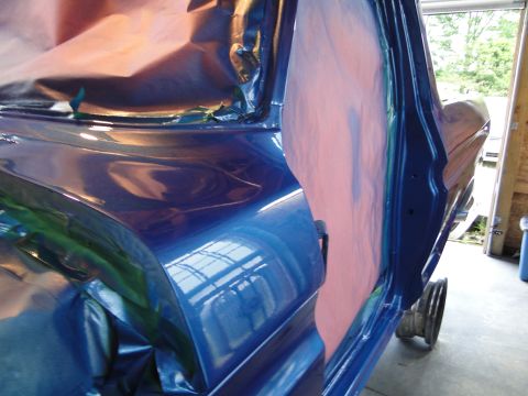 1978 Ford Bronco - Vehicle body panels are masked and painted blue, with reflections of a workshop ceiling visible.