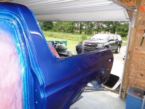 1978 Ford Bronco - A vehicle body, likely undergoing a fresh paint job, is visible in the foreground of this garage scene, with an SUV parked outside.