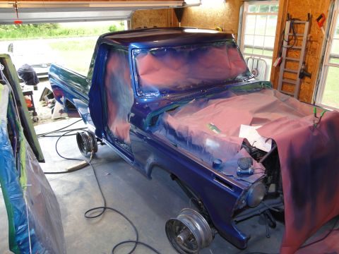 1978 Ford Bronco - A blue Ford truck is being prepped for a new paint job inside a garage, with its wheels removed.