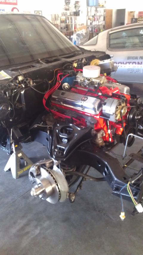 1973 Chevrolet Camaro - Car engine bay with chrome valve covers and red wiring, supported by jack stands, with another vehicle visible in the background.