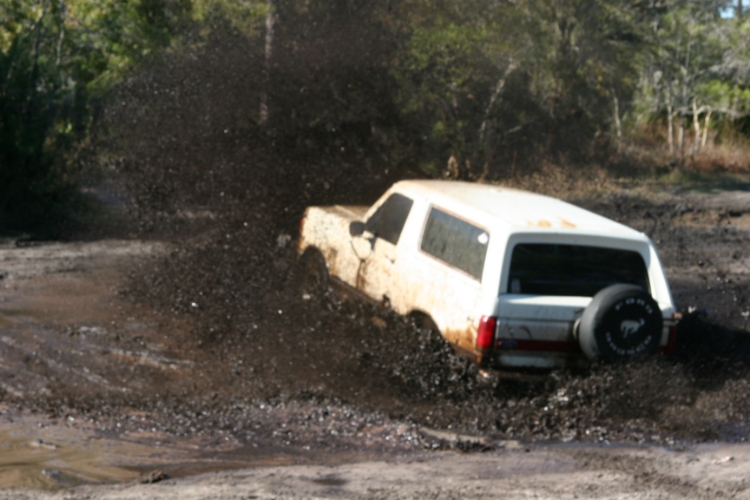 white 1988 Ford Bronco driving through mud