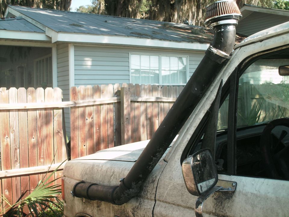 Custom black snorkel intake with cone air filter mounted on hood of a dusty van